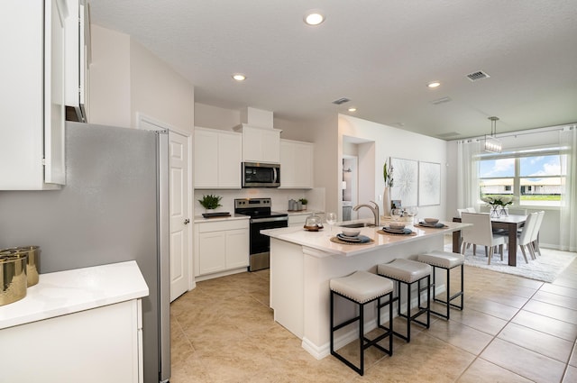 kitchen with pendant lighting, white cabinetry, stainless steel appliances, and a kitchen island with sink