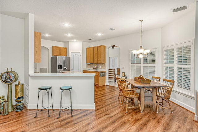 kitchen featuring a notable chandelier, kitchen peninsula, light wood-type flooring, and stainless steel refrigerator with ice dispenser