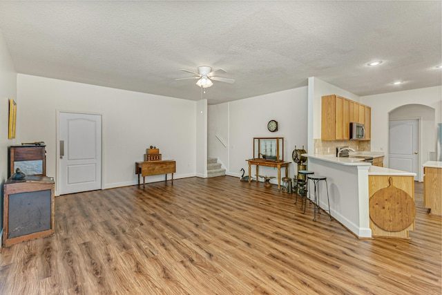 interior space with ceiling fan, a kitchen breakfast bar, light hardwood / wood-style flooring, kitchen peninsula, and appliances with stainless steel finishes