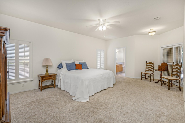 bedroom featuring multiple windows, ceiling fan, ensuite bathroom, and light carpet