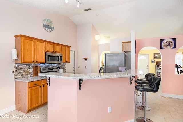 kitchen featuring a breakfast bar, appliances with stainless steel finishes, lofted ceiling, and an island with sink