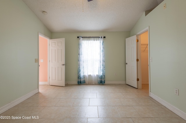 tiled spare room featuring lofted ceiling and a textured ceiling