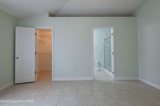 unfurnished bedroom featuring lofted ceiling, light tile patterned floors, a textured ceiling, a spacious closet, and a closet