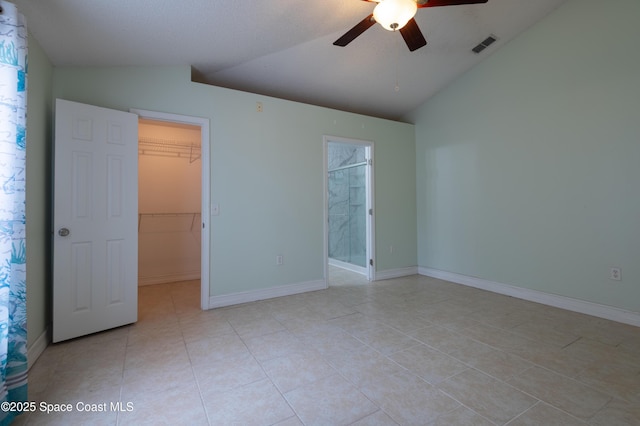 unfurnished bedroom featuring light tile patterned flooring, lofted ceiling, a walk in closet, ceiling fan, and a closet