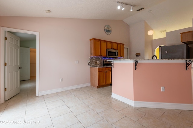 kitchen with appliances with stainless steel finishes, a kitchen breakfast bar, light tile patterned flooring, decorative backsplash, and vaulted ceiling