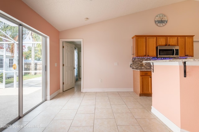 kitchen with light tile patterned floors, tasteful backsplash, a textured ceiling, a kitchen bar, and vaulted ceiling