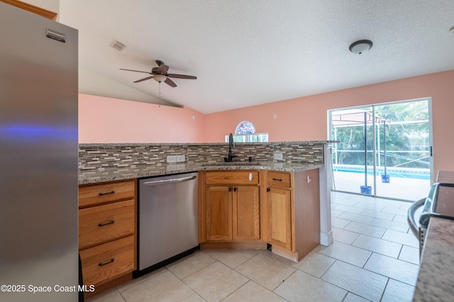 kitchen featuring sink, stainless steel appliances, light stone counters, decorative backsplash, and vaulted ceiling