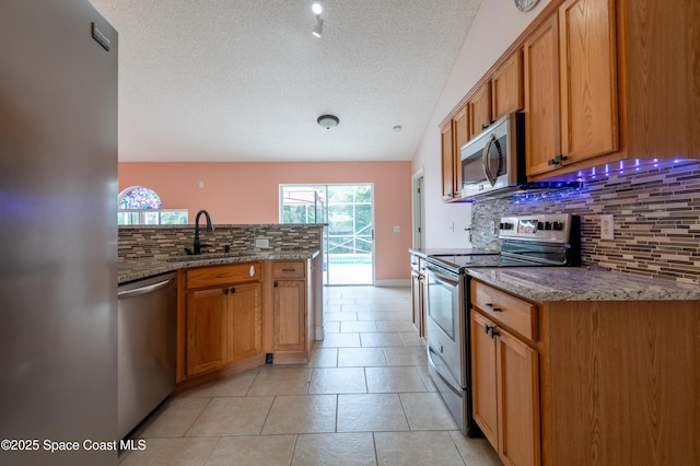 kitchen with tasteful backsplash, appliances with stainless steel finishes, sink, and light stone counters