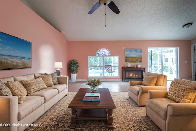 living room featuring ceiling fan, vaulted ceiling, tile patterned floors, and a textured ceiling