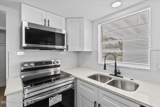 kitchen featuring white cabinets, sink, decorative backsplash, light stone countertops, and appliances with stainless steel finishes