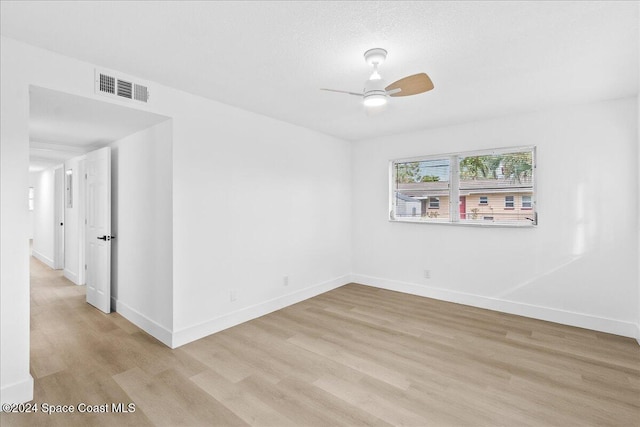 unfurnished room with a textured ceiling, light wood-type flooring, and ceiling fan