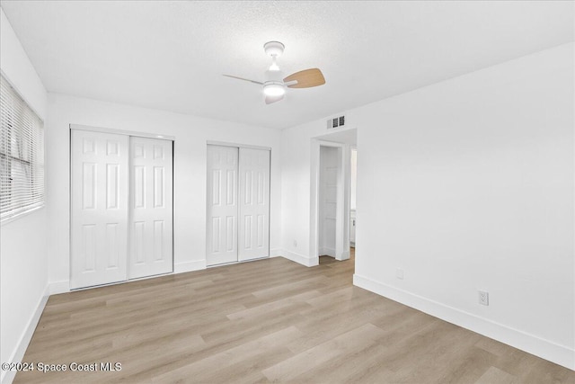 unfurnished bedroom with multiple closets, ceiling fan, light hardwood / wood-style floors, and a textured ceiling