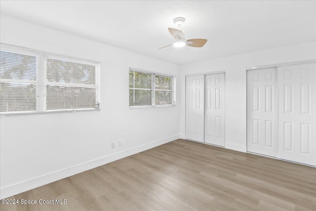 unfurnished bedroom with ceiling fan, light hardwood / wood-style floors, and multiple closets