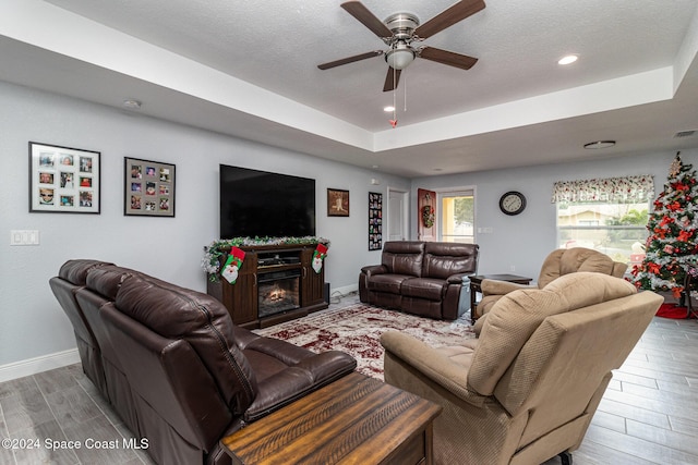 living room with ceiling fan, a raised ceiling, light wood-type flooring, and a textured ceiling