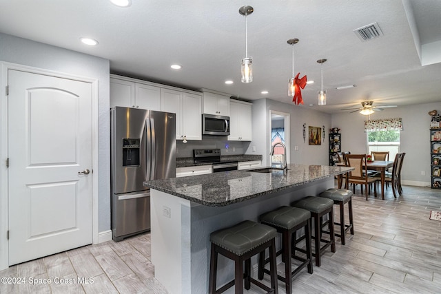 kitchen featuring a kitchen island with sink, sink, dark stone countertops, white cabinetry, and stainless steel appliances