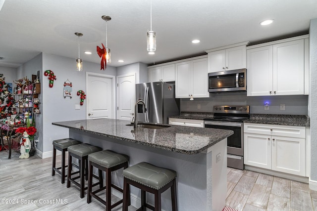 kitchen with appliances with stainless steel finishes, light hardwood / wood-style floors, white cabinetry, and an island with sink