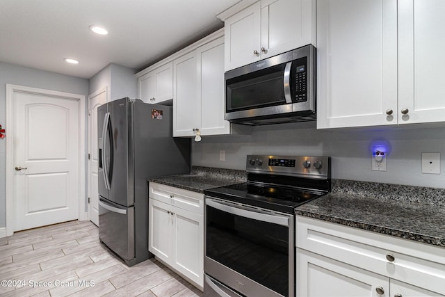 kitchen featuring dark stone counters, white cabinetry, stainless steel appliances, and light wood-type flooring