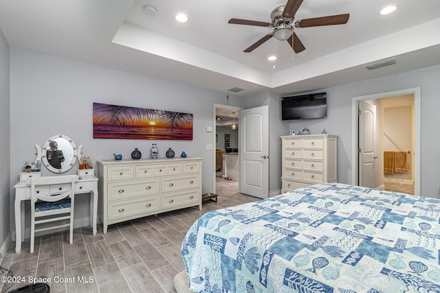 bedroom with ceiling fan, light wood-type flooring, and a tray ceiling