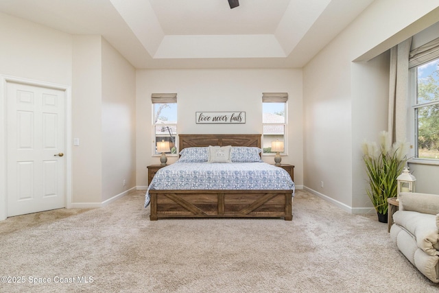 carpeted bedroom featuring ceiling fan, multiple windows, and a tray ceiling