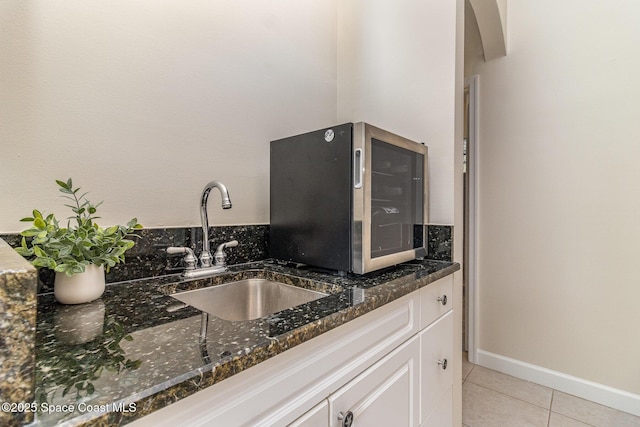 kitchen featuring sink, light tile patterned floors, white cabinetry, and dark stone counters