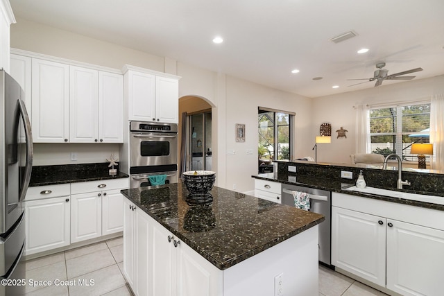 kitchen featuring appliances with stainless steel finishes, a center island, white cabinetry, dark stone countertops, and sink