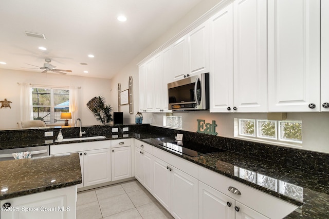 kitchen featuring appliances with stainless steel finishes, sink, white cabinetry, light tile patterned floors, and dark stone counters