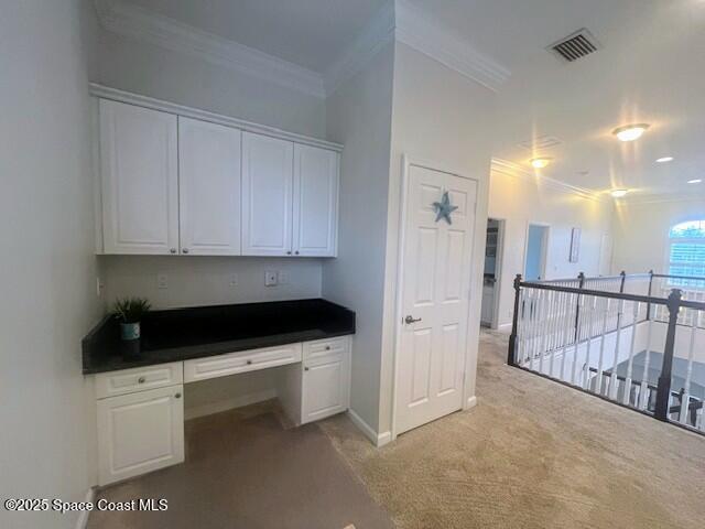 unfurnished office featuring ornamental molding, light colored carpet, and built in desk