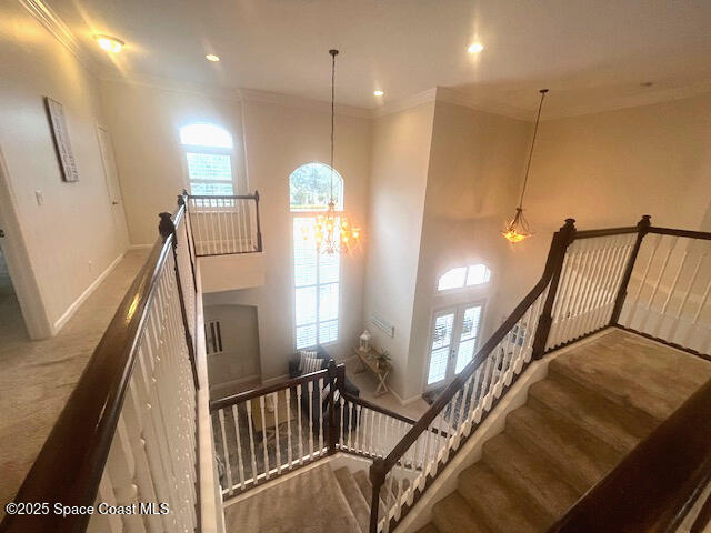 staircase featuring a notable chandelier, ornamental molding, and plenty of natural light