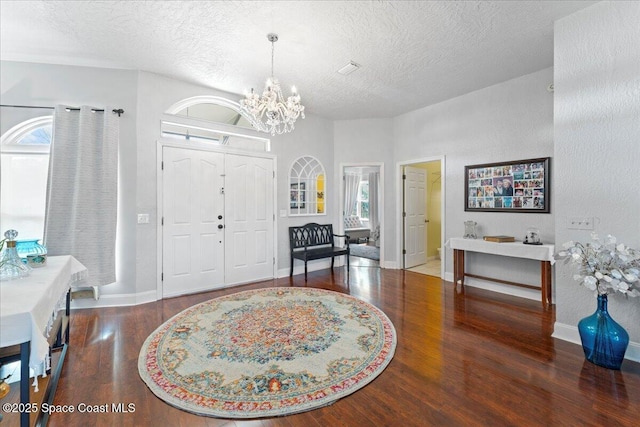 foyer with an inviting chandelier, dark wood-type flooring, and a textured ceiling