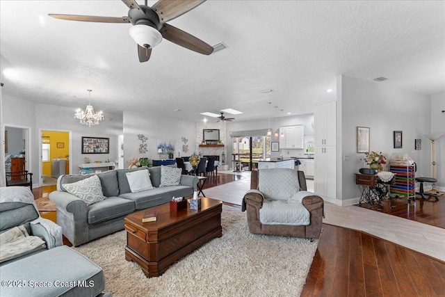 living room featuring ceiling fan with notable chandelier, a large fireplace, light hardwood / wood-style floors, and a textured ceiling