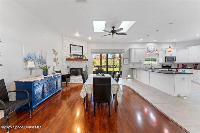 dining room featuring sink, ceiling fan, a skylight, a fireplace, and light hardwood / wood-style floors