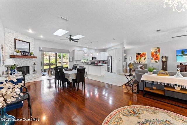 dining area with wood-type flooring, a stone fireplace, a skylight, and a textured ceiling