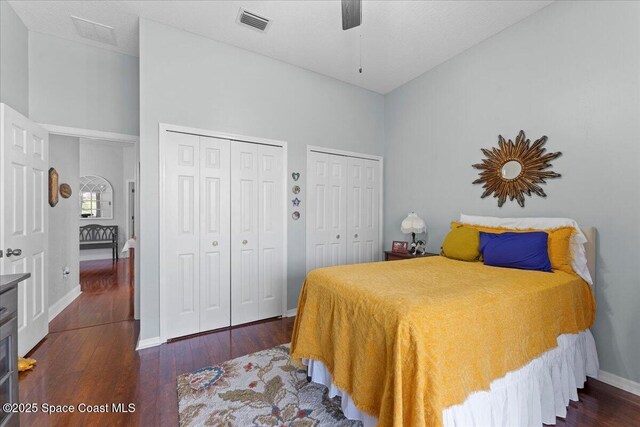 bedroom featuring dark hardwood / wood-style floors, two closets, ceiling fan, and a towering ceiling