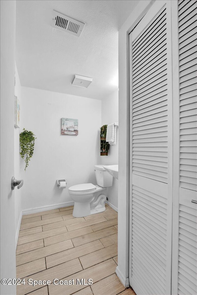 bathroom featuring wood-type flooring, a textured ceiling, and toilet