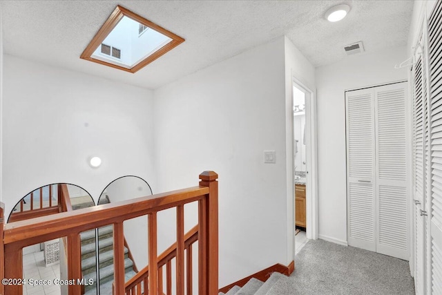 hall with a textured ceiling, light carpet, and a skylight