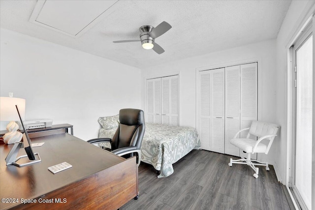 bedroom with a textured ceiling, dark hardwood / wood-style flooring, ceiling fan, and multiple closets