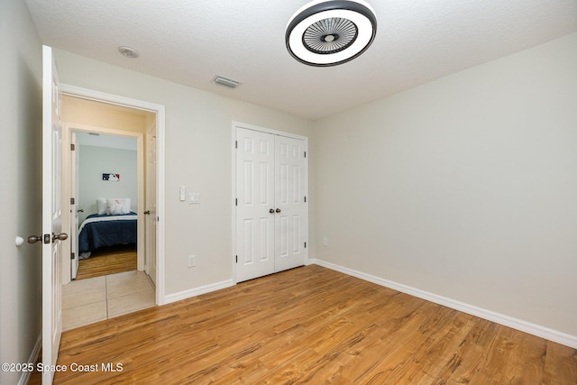 unfurnished bedroom with a textured ceiling, a closet, and light hardwood / wood-style flooring