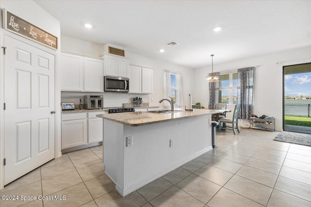 kitchen with light stone counters, white cabinetry, a kitchen island with sink, and hanging light fixtures