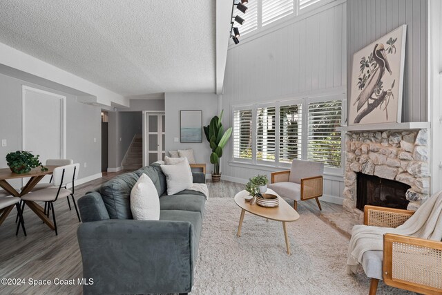 living room with lofted ceiling, a stone fireplace, wood-type flooring, and a textured ceiling