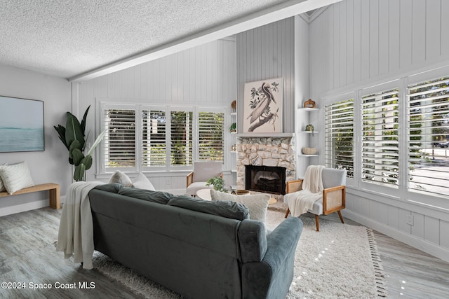 living room with a stone fireplace, wooden walls, a textured ceiling, and hardwood / wood-style flooring