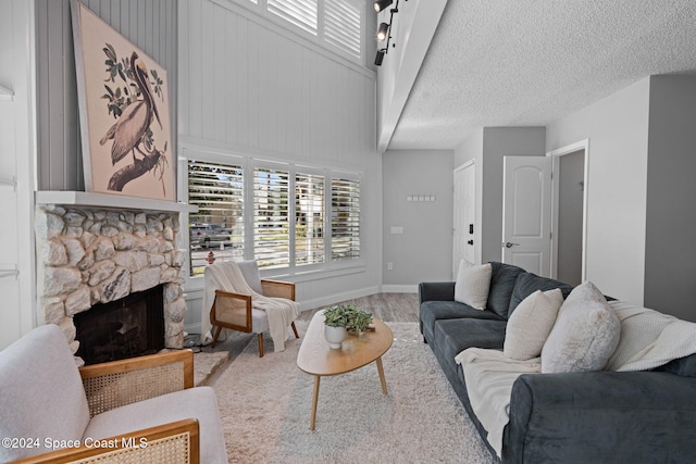 living room featuring a stone fireplace, a textured ceiling, and high vaulted ceiling