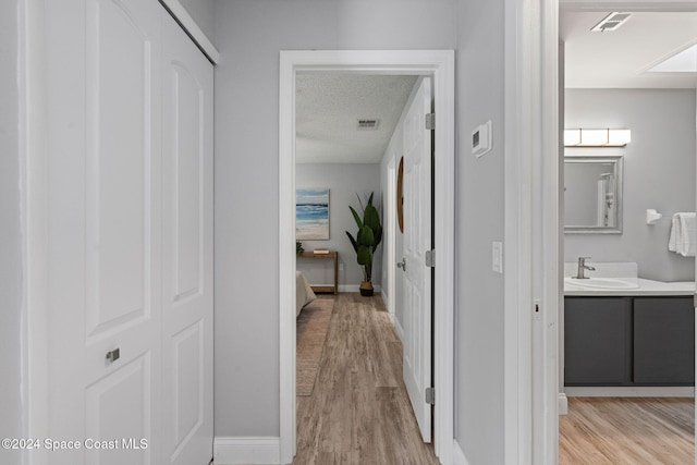 hallway with a textured ceiling, light hardwood / wood-style floors, and sink