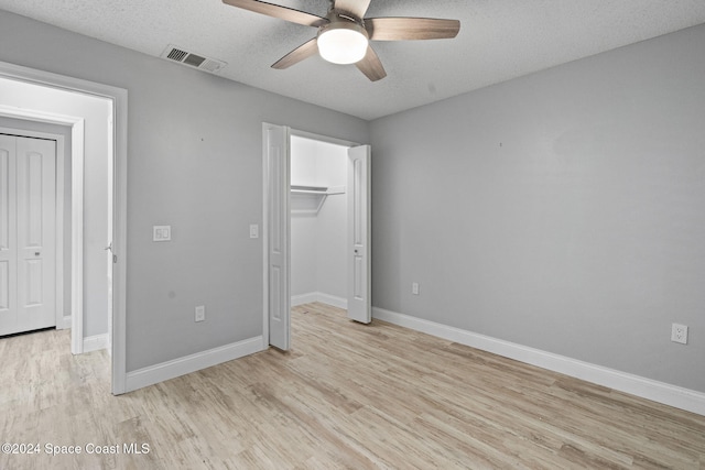 unfurnished bedroom featuring ceiling fan, a spacious closet, light wood-type flooring, a textured ceiling, and a closet