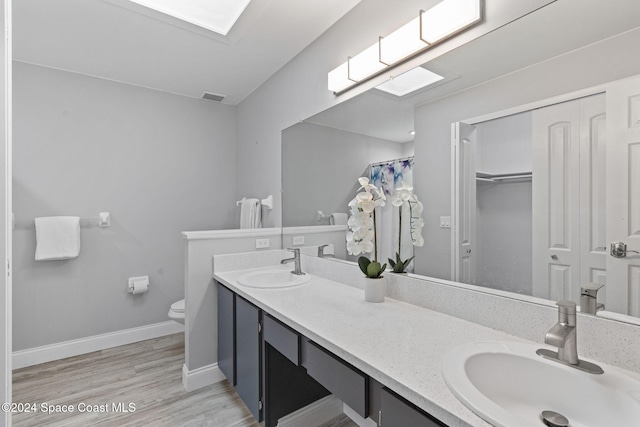 bathroom featuring vanity, toilet, wood-type flooring, and a skylight