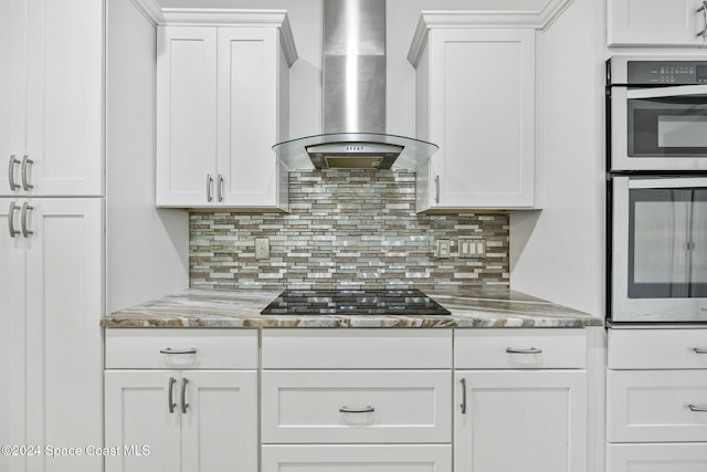 kitchen featuring backsplash, black gas stovetop, double oven, wall chimney range hood, and white cabinets