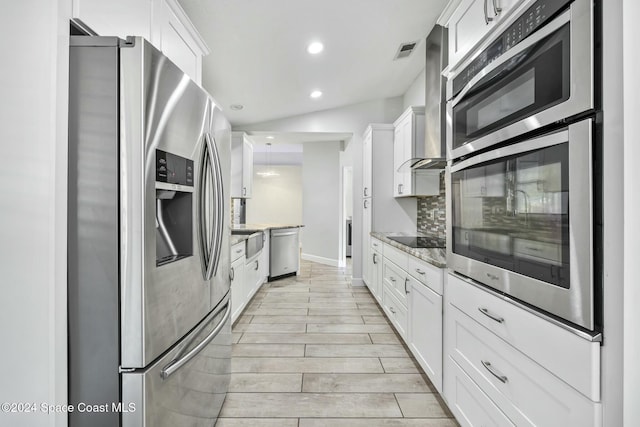 kitchen featuring light stone countertops, backsplash, lofted ceiling, white cabinets, and appliances with stainless steel finishes