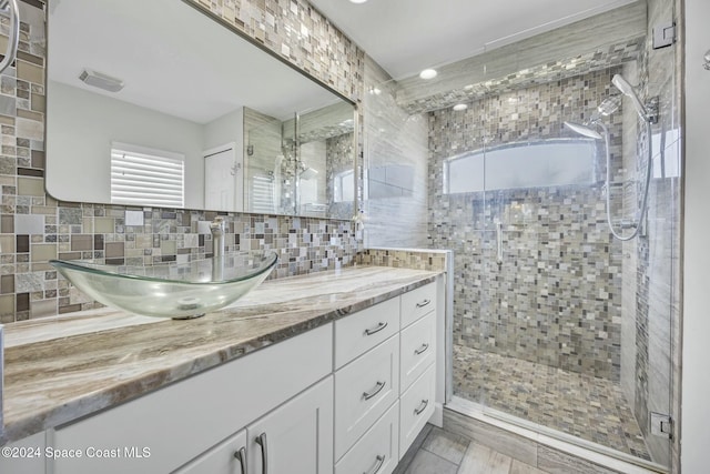 bathroom featuring vanity, backsplash, a shower with door, and a wealth of natural light