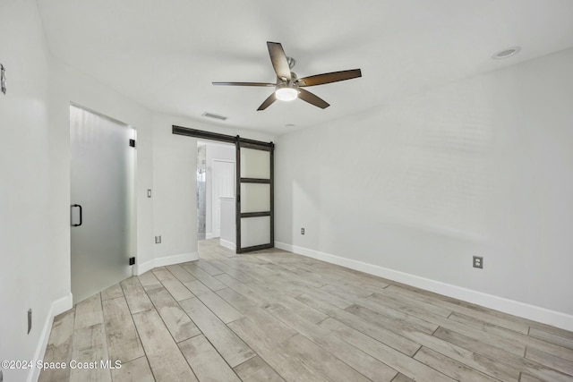 unfurnished room with a barn door, ceiling fan, and light hardwood / wood-style flooring