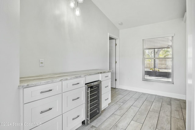 kitchen with white cabinets, vaulted ceiling, light stone countertops, light wood-type flooring, and beverage cooler