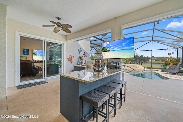 view of patio featuring ceiling fan, a lanai, exterior bar, and an outdoor kitchen